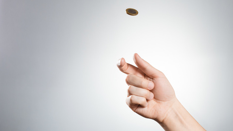 Eine Hand wirft eine Münze vor grauem Hintergrund